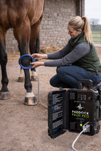 Person using a Paddock Pulse Pro device on a horse's leg in an outdoor setting.